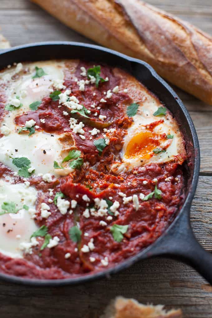 Shakshuka with harissa in a cast-iron pan next to a french baguette