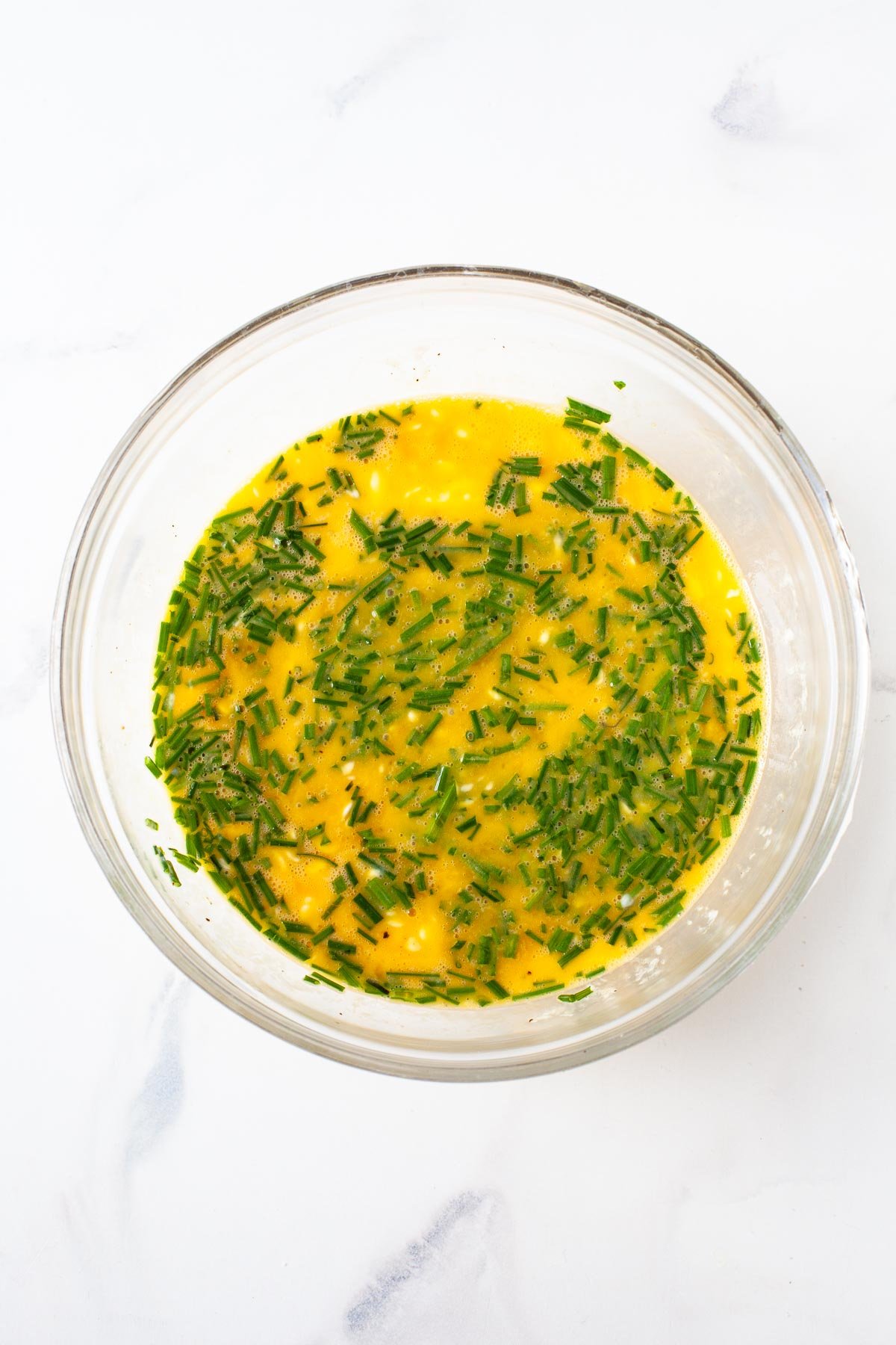 eggs and yogurt whisked in glass bowl with chopped chives on top