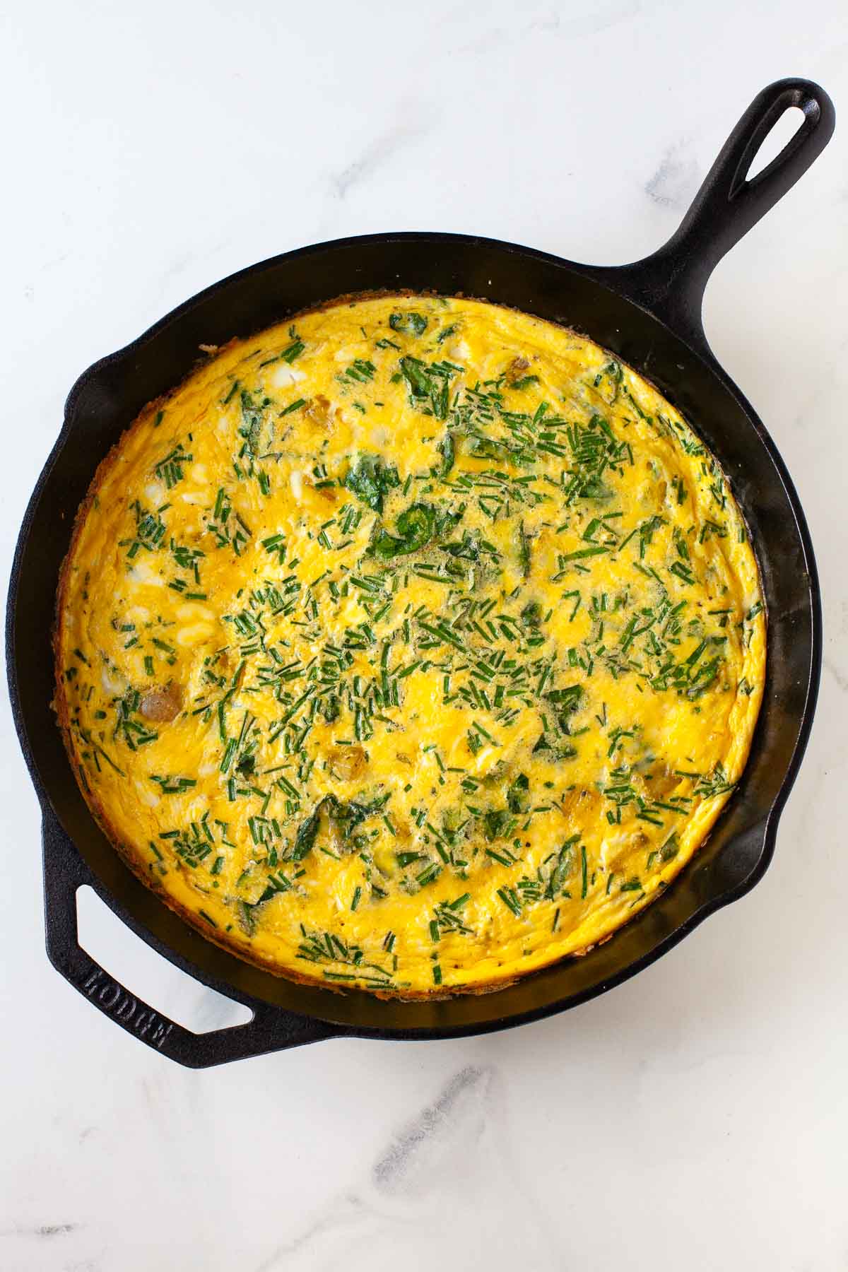 cooked swiss chard potato and chive frittata in black cast iron pan on marble surface
