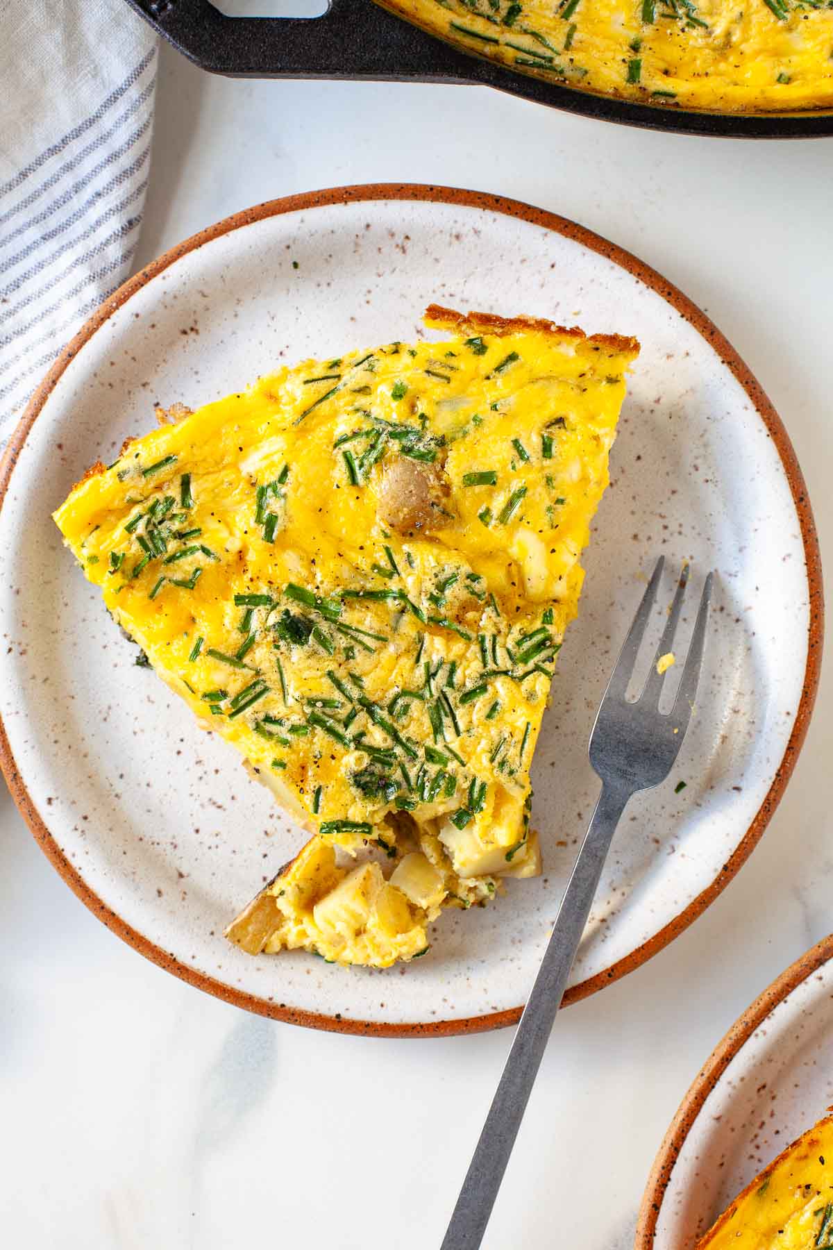 slice of potato swiss chard chive frittata with bite taken out and fork on speckled plate
