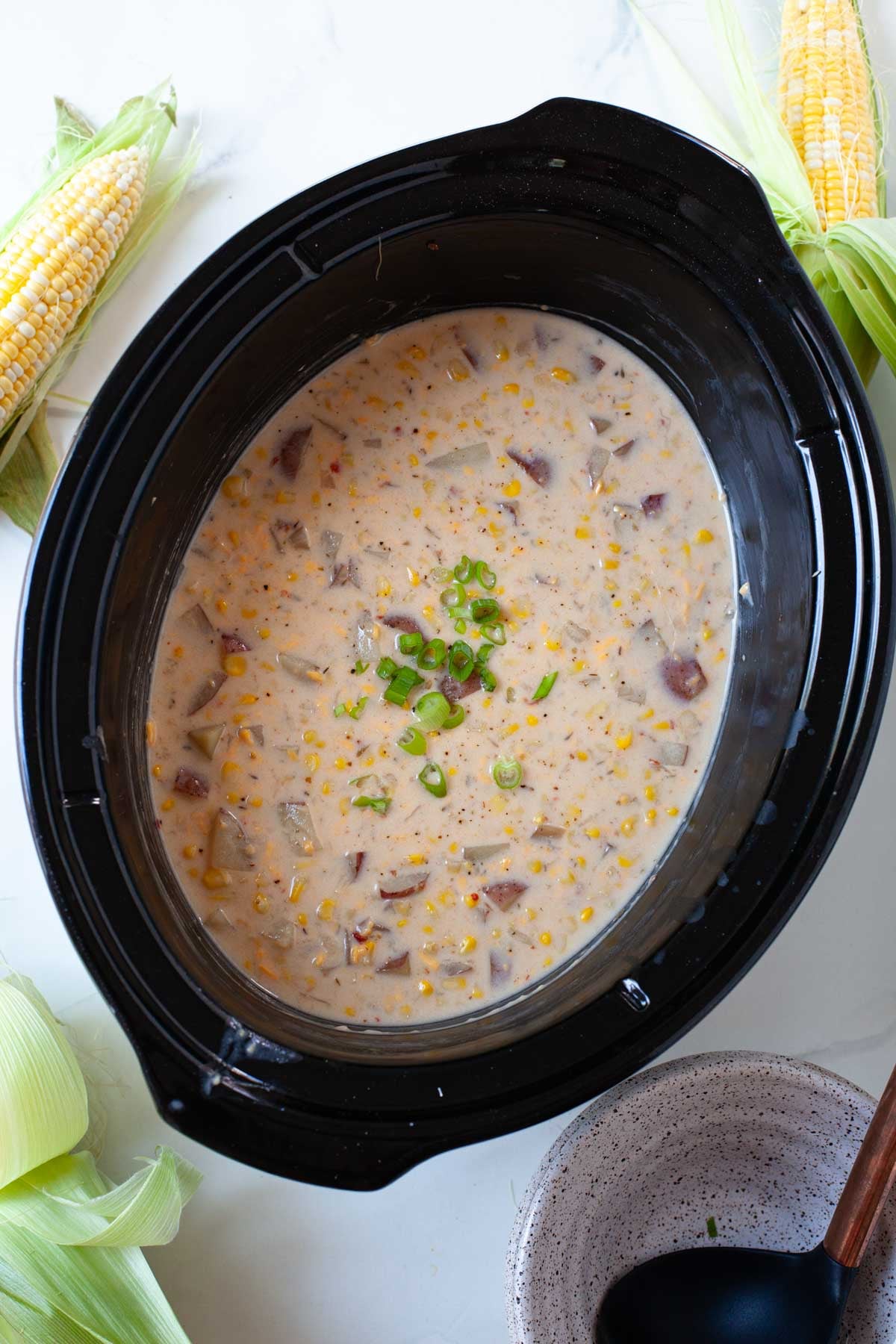 creamy corn potato chowder with green onion garnish in black slow cooker