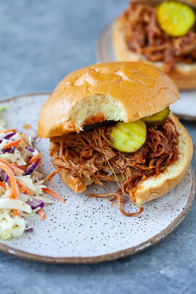 pulled BBQ chicken on bun with pickles and bite missing on a plate with coleslaw TeamJiX
