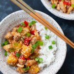 sweet and sour chicken over a bed of white rice in a bowl on a dark background