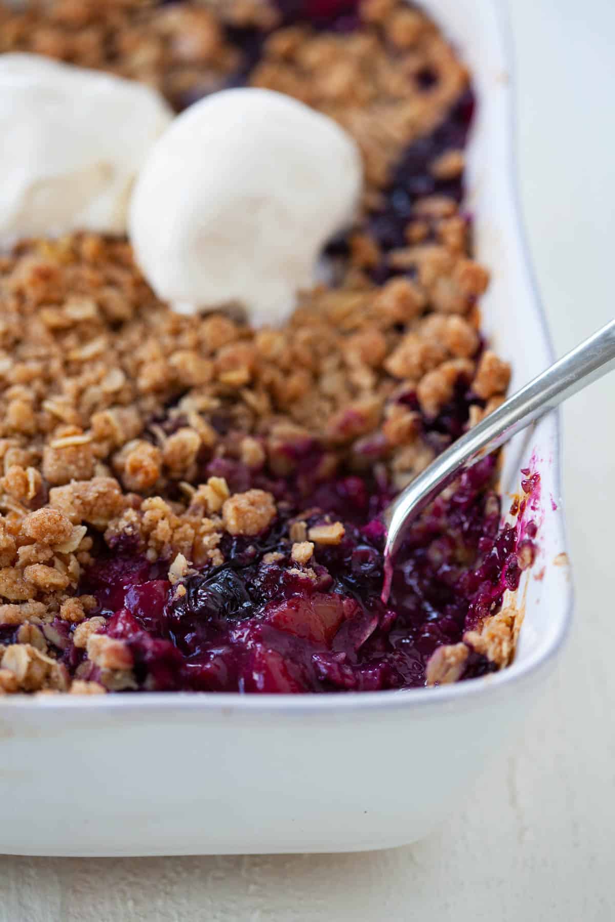 Blueberry Peach Basil Crisp in a white baking dish with a serving spoon