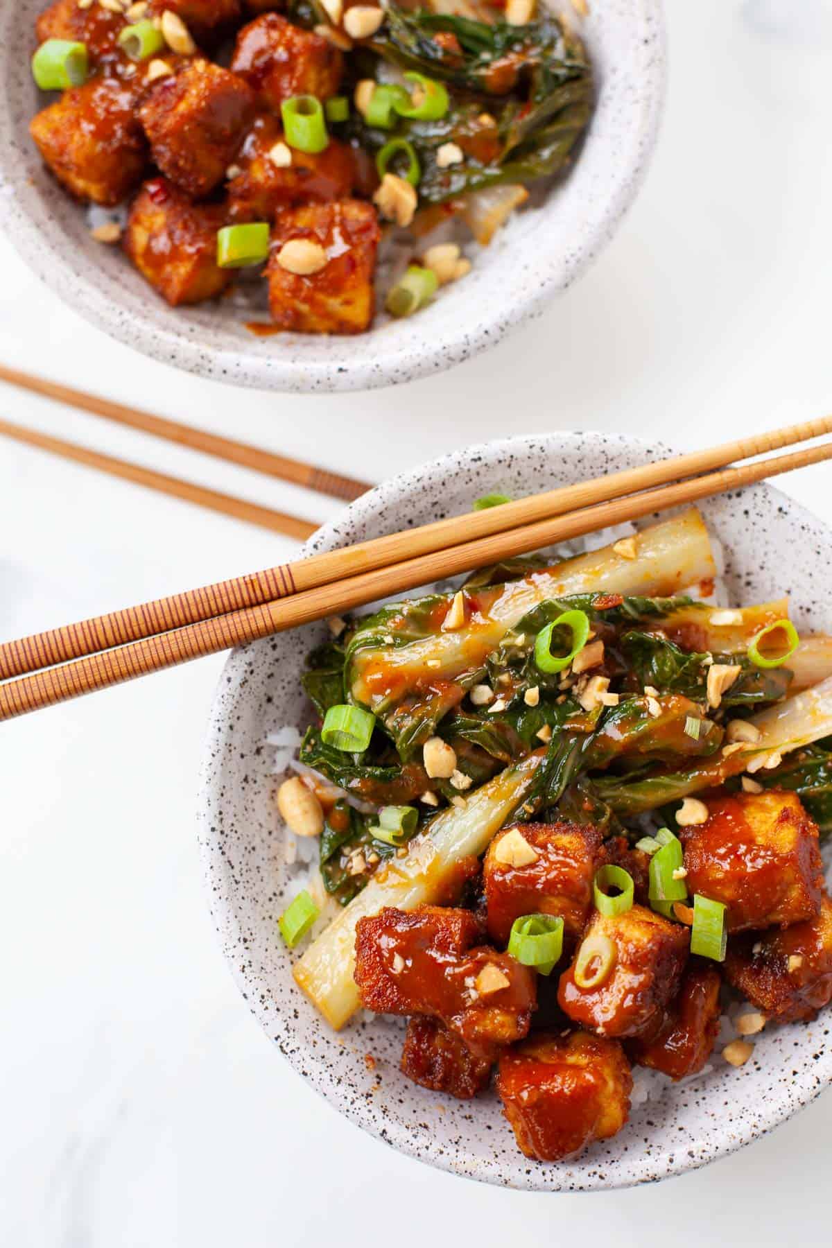 two tofu rice bowls with bok choy, scallions, and crushed peanuts in a bowl with chopsticks