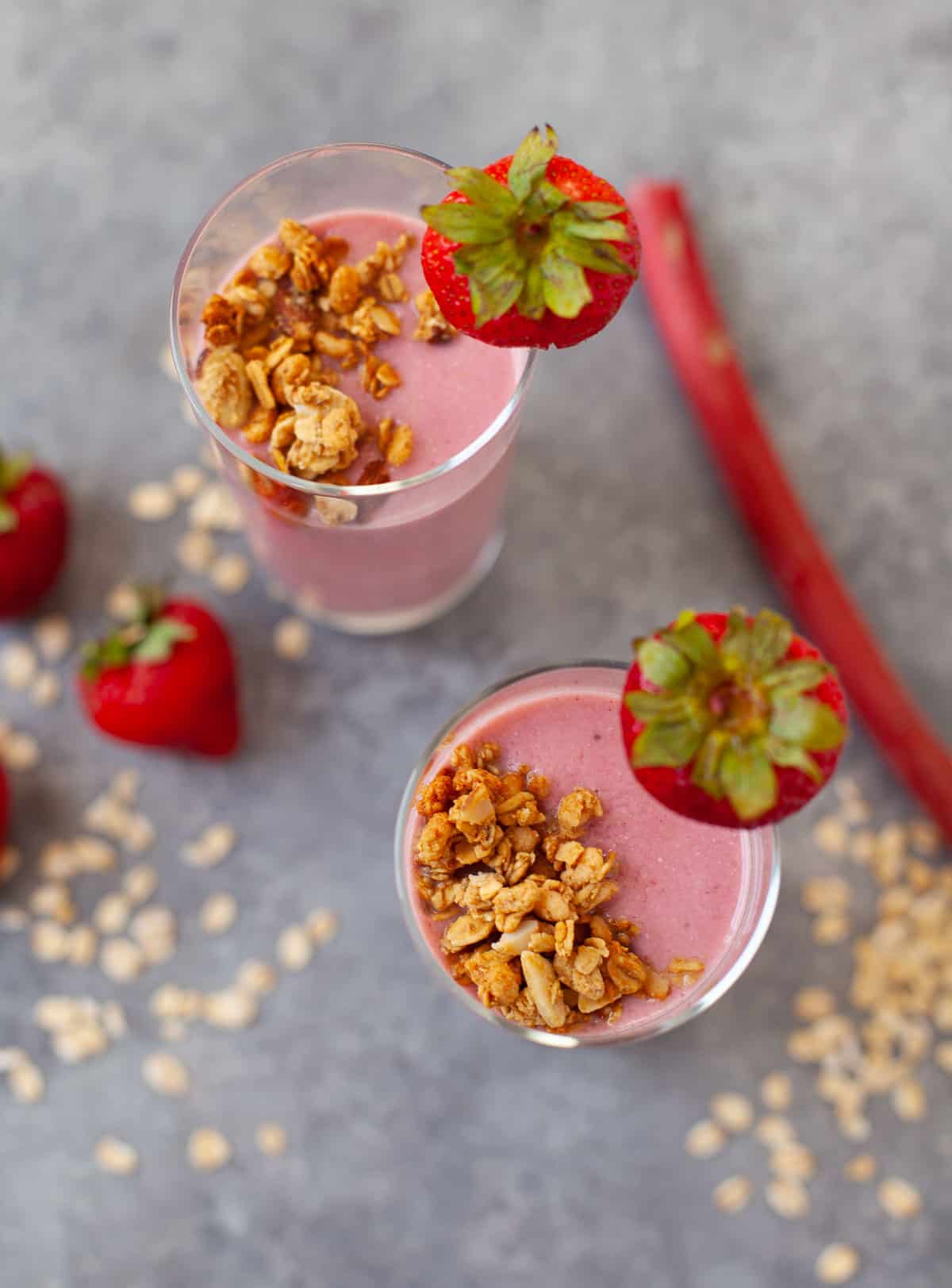 two glasses of strawberry rhubarb pie smoothie with fresh strawberries and granola for garnish