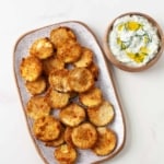 crispy zucchini chips on a plate next to a bowl of dip