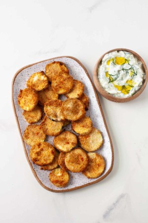 crispy zucchini chips on a plate next to a bowl of dip