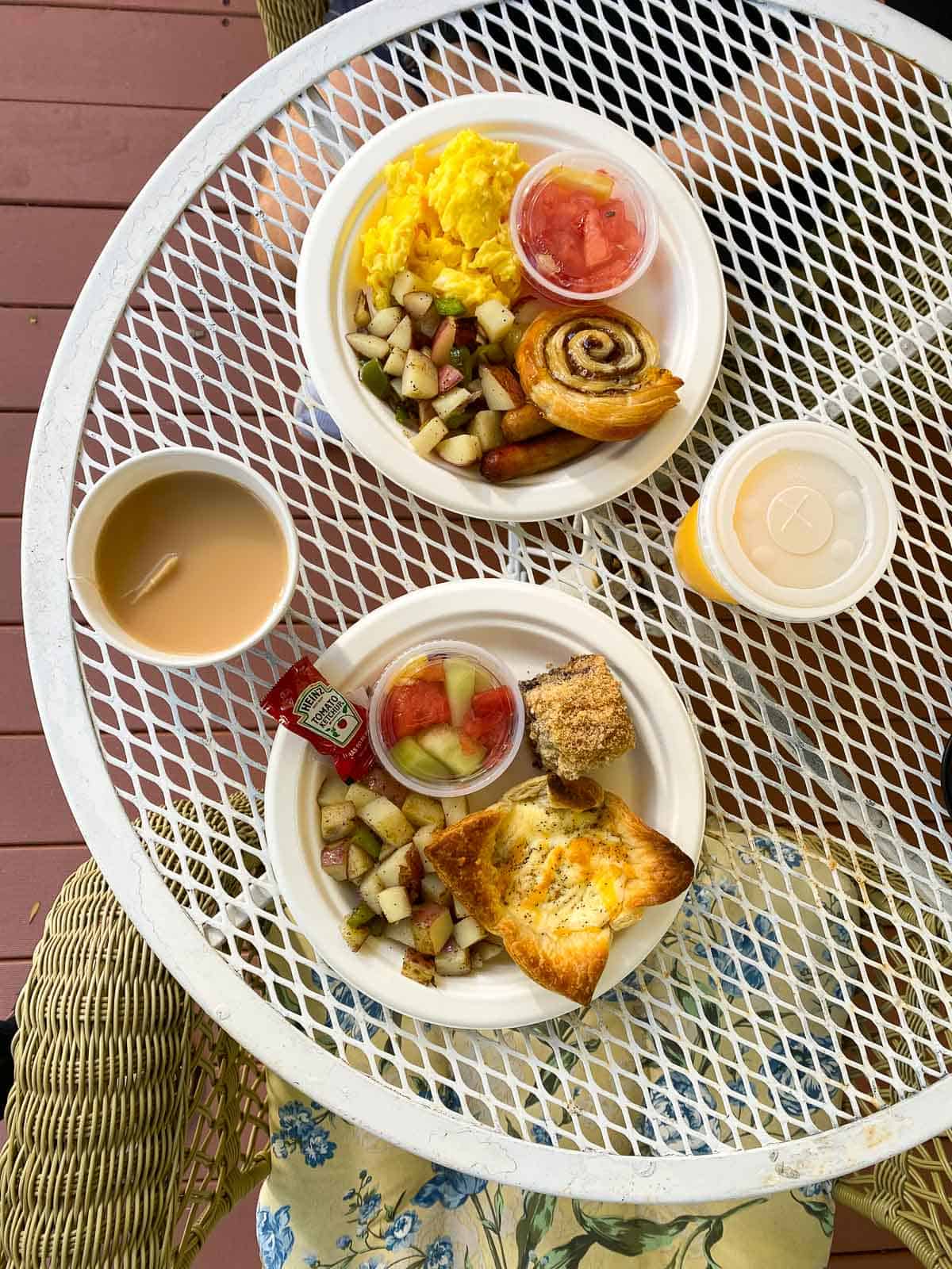 two plates full of breakfast items like scrambled eggs, potatos, a cinnamon roll, and a muffin