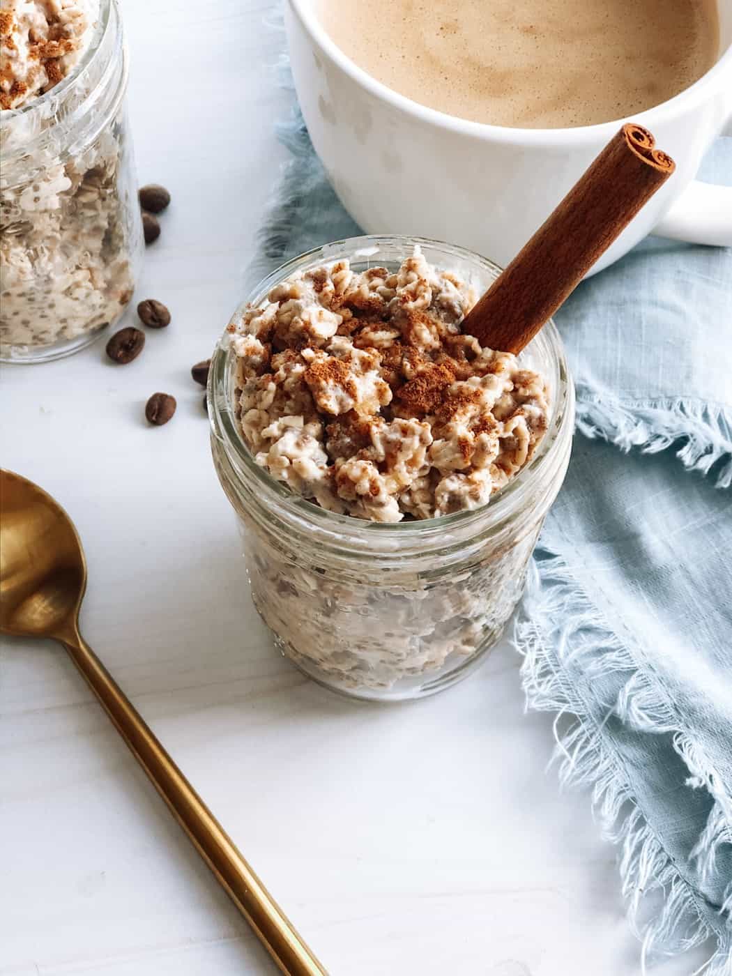Mason jar filled with chai spiced overnight oats with stick of cinnamon and cup of coffee