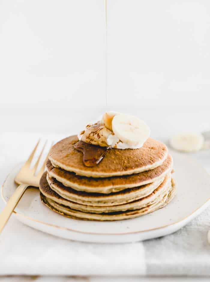 stack of banana chai pancakes with sliced bananas on top and syrup being poured over pancakes