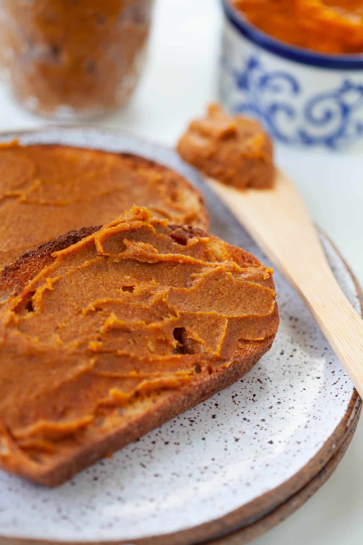 wooden spoon with pumpkin almond butter spread out on two slices of toast