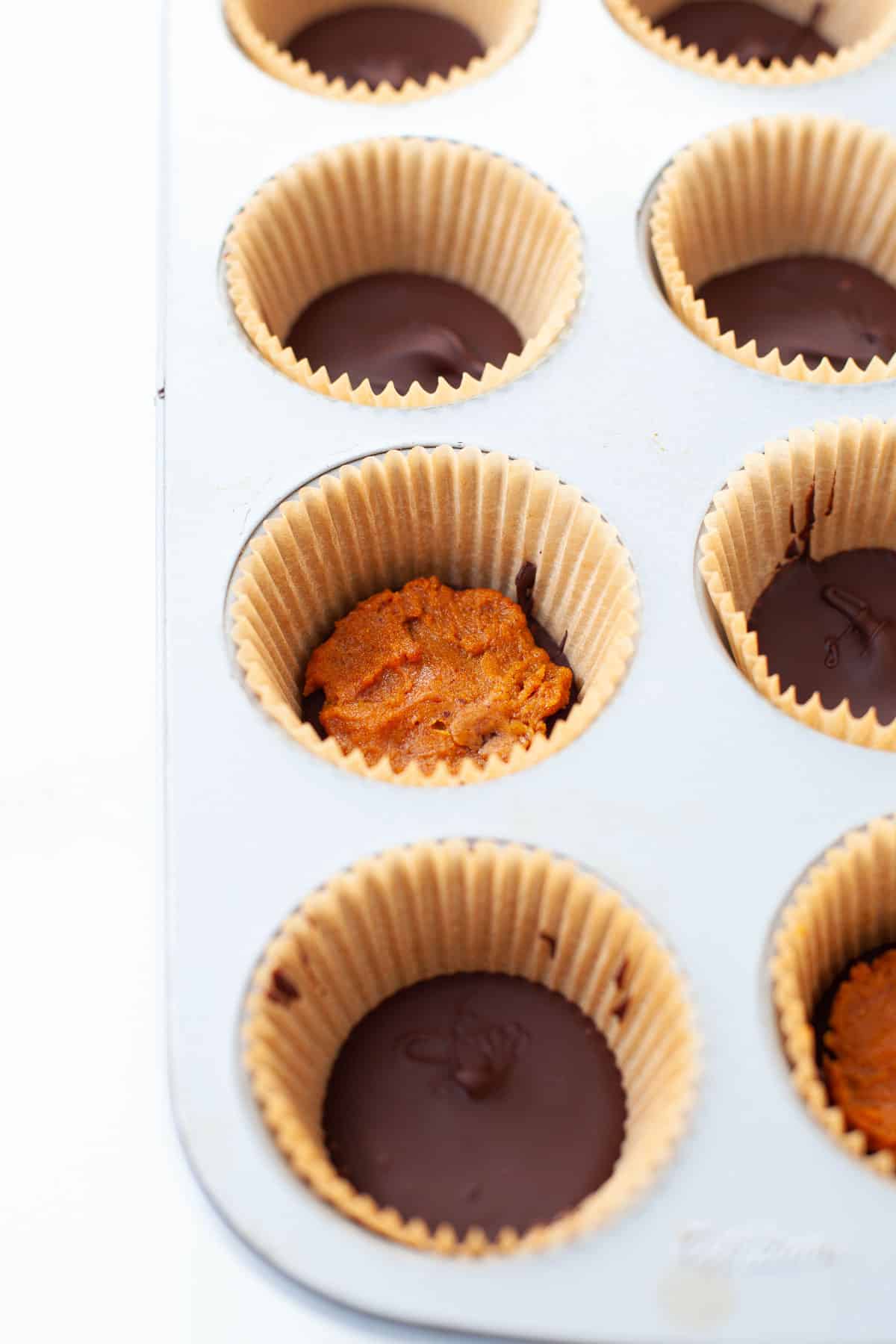 scoop of almond butter placed on top of dark chocolate laying in bottom of cupcake wrapper