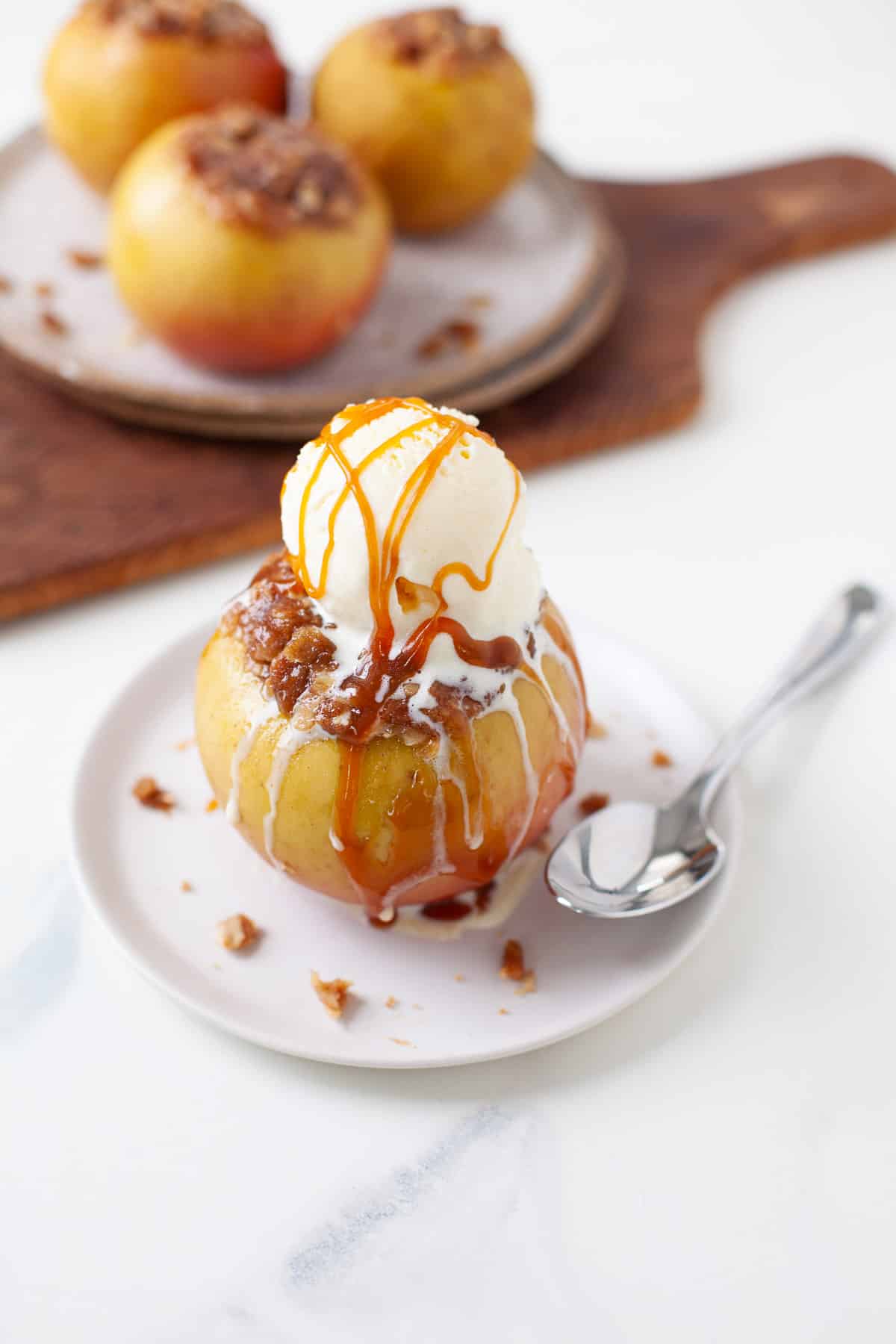 baked apple with cinnamon oat mixture with scoop of vanilla ice cream and caramel drizzle with three baked apples in foreground