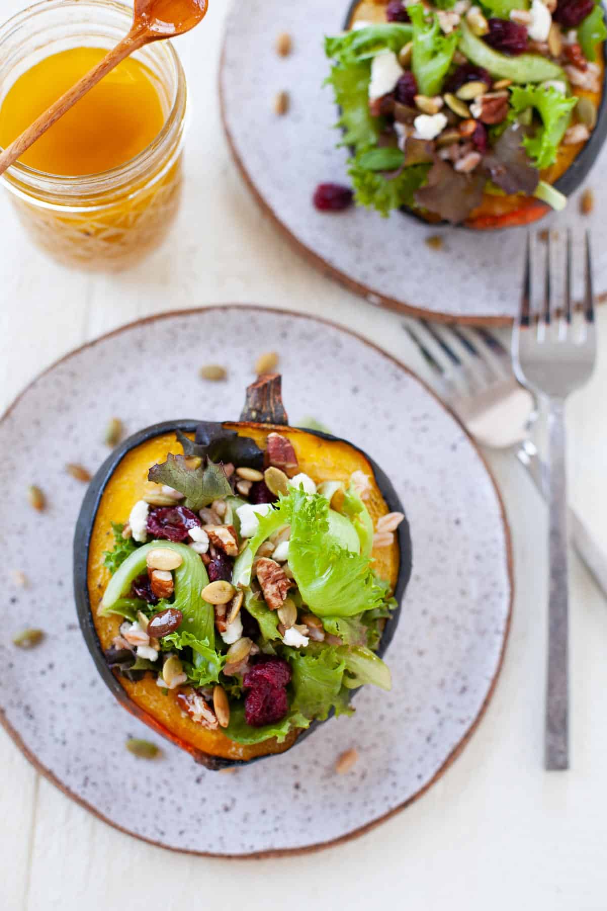 two servings of acorn squash stuffed with baby springs, dried cranberries, goat cheese, pecans, and pepitas