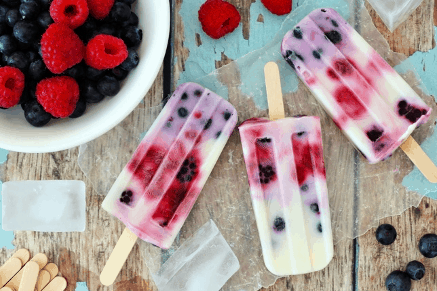 three popsicles laid out on apicnic table next to a bowl of berries