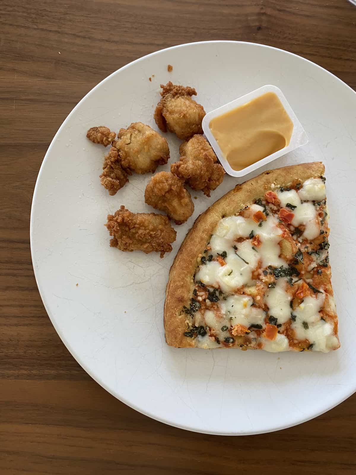 chicken nuggets with sauce and slice of pizza on white plate on wood table
