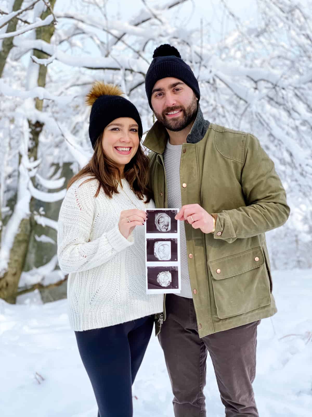 couple with pregnancy announcement holding sonogram pictures with winter snow in background