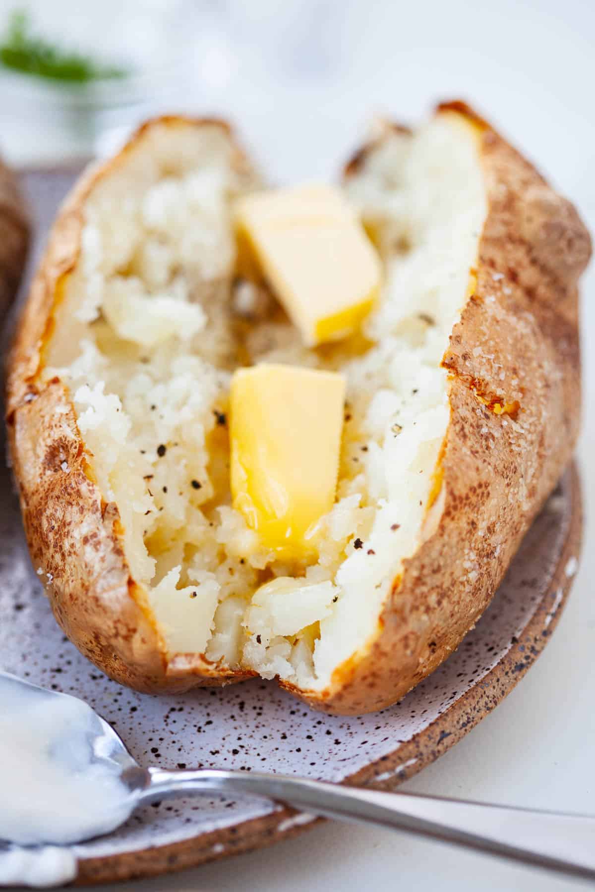 baked potato that's sliced in half with butter melting in the middle and pepper sprinkled on top