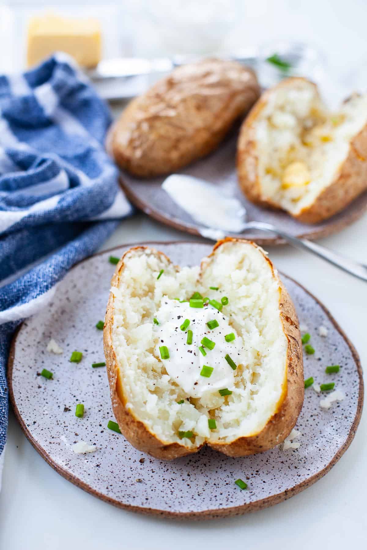 baked potato that's sliced in half with sour cream and two baked potatoes on another plate