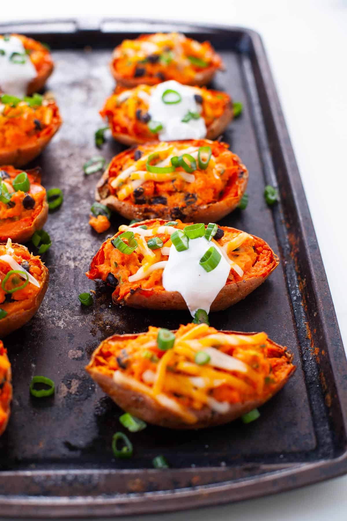 two rows of sweet potato skins on a sheet pan with scallions and melted vegan cheese