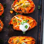 four sweet potato skins with vegan cheese and sliced scallions laid out on a sheet pan