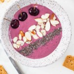 cherry cheesecake smoothie bowl with cherries, almonds, chia seeds in grey speckled bowl with graham crackers