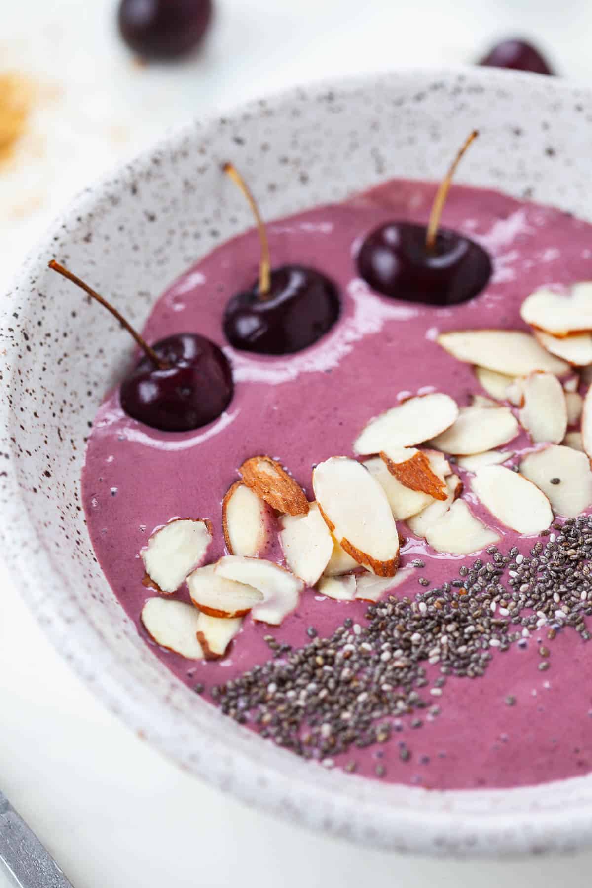 close up of cherry cheesecake smoothie bowl in grey bowl with cherries, almonds, chia seeds