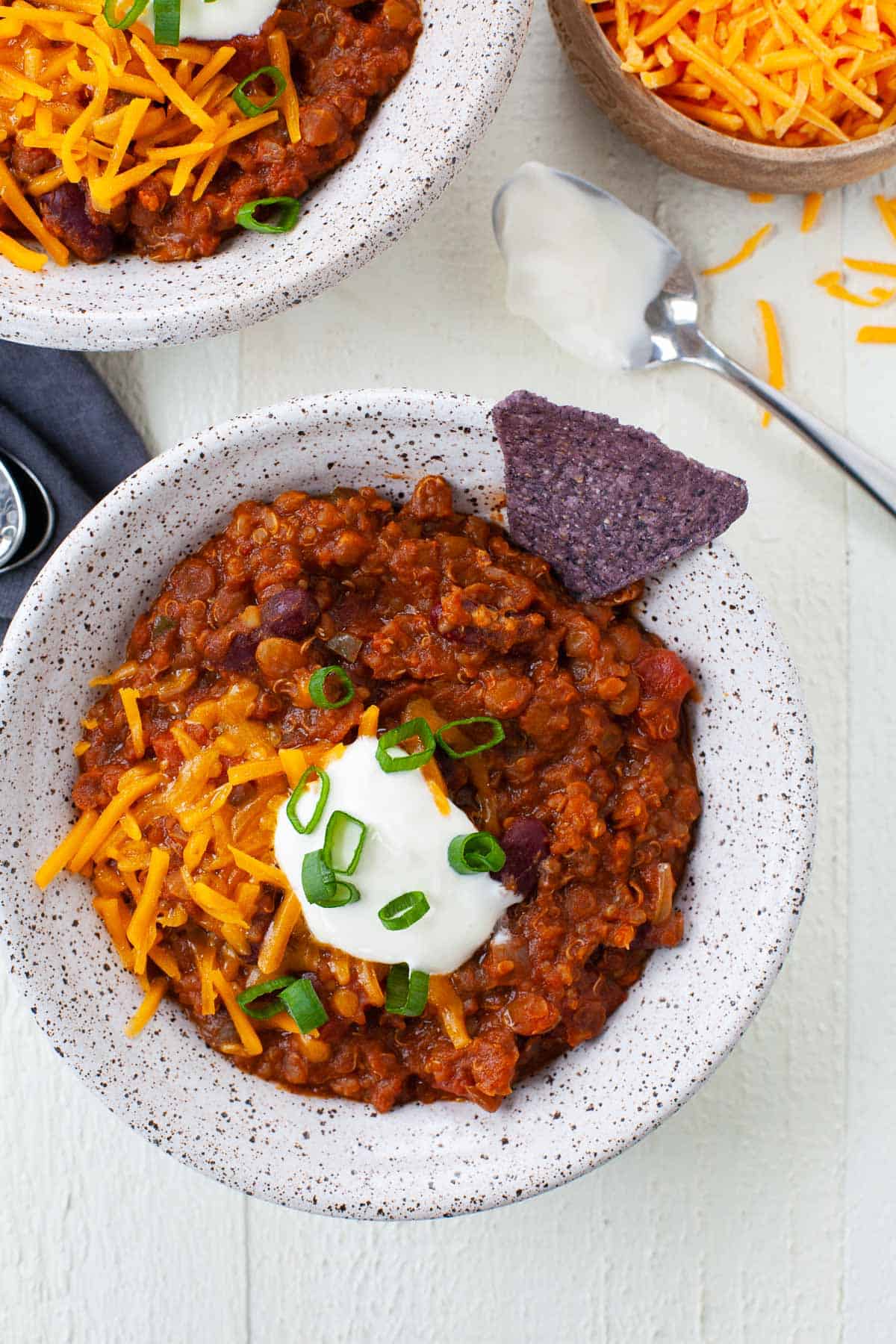 bowls of vegetarian chili with tortilla chip, cheese, sour cream, scallions and spoon with sour cream