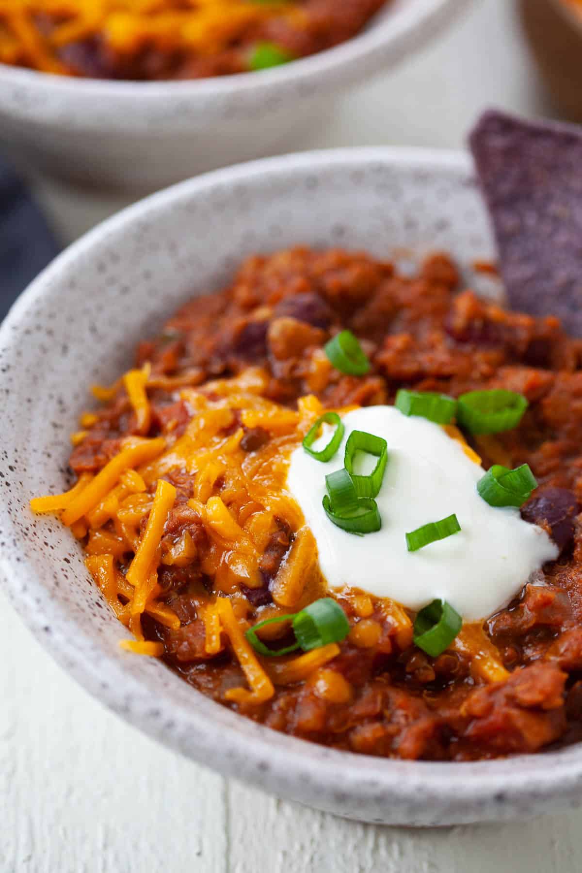 close up of instant pot vegetarian chili in grey bowl with cheese, sour cream, scallions