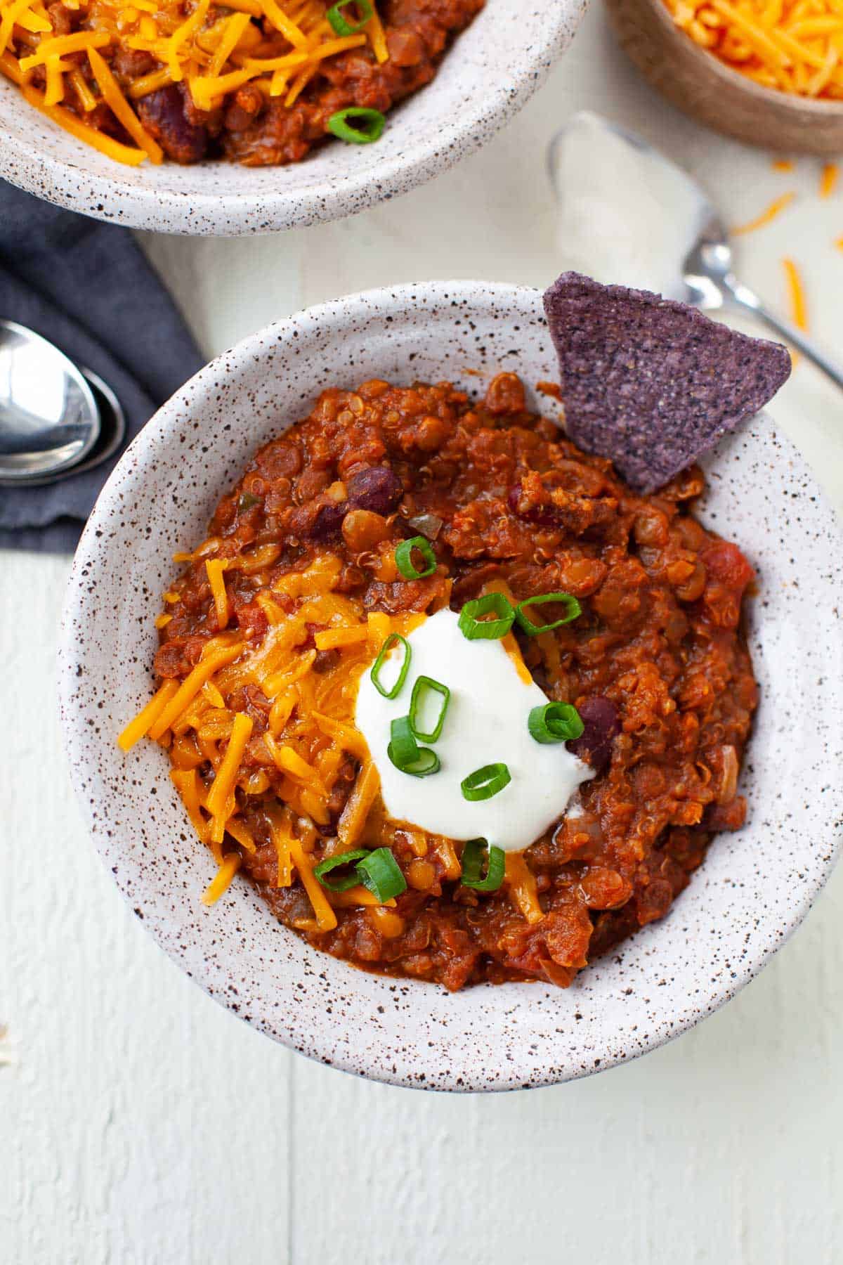 bowl of vegetarian chili with tortilla chip, cheese, sour cream, and scallions on white surface