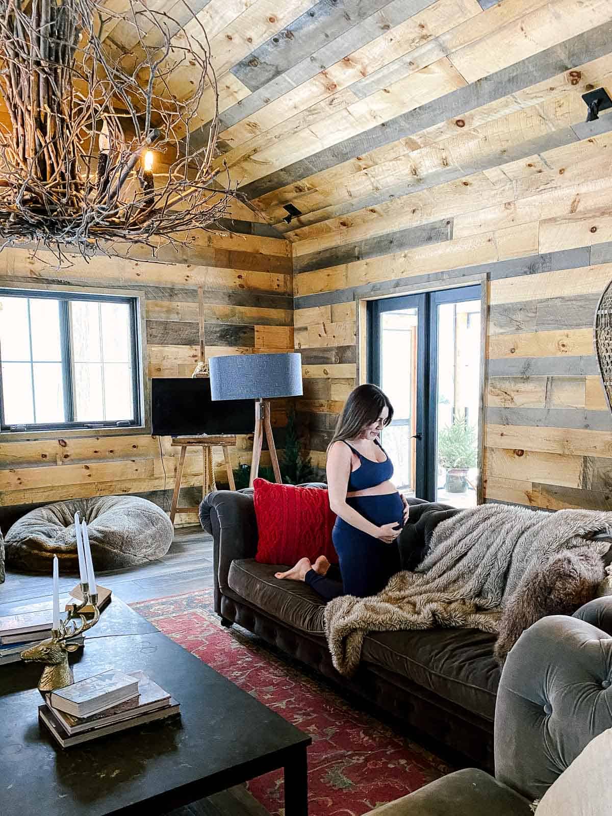 pregnant woman in yoga clothes on couch in cabin with wood walls and rustic chandelier 