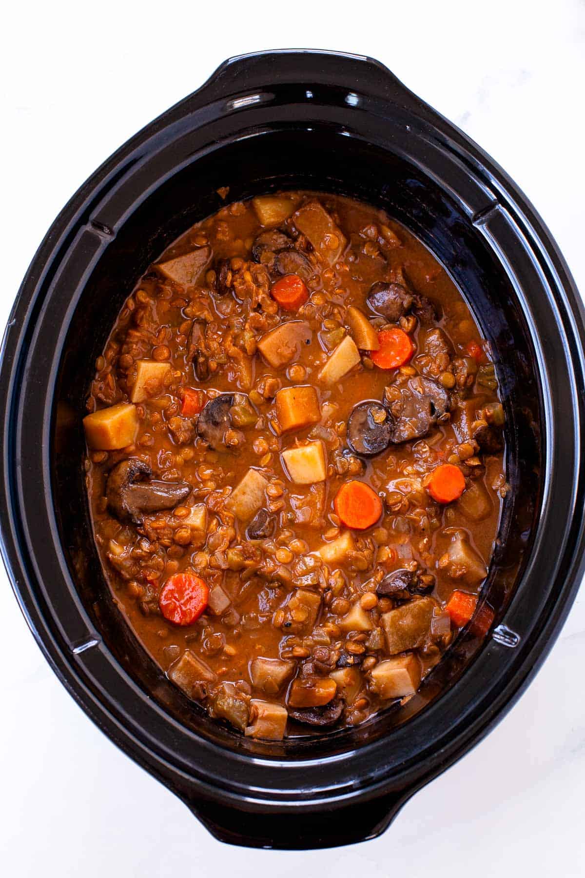 up close vegetarian irish stew with carrots, lentil, mushroom, celery in black slow cooker