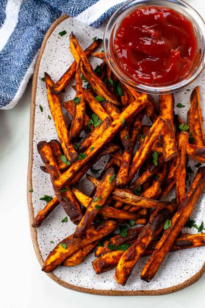 crispy sweet potato fries next to a bowl of ketchup, cilantro garnish