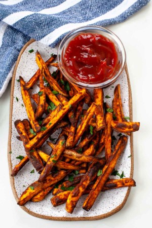 air fryer sweet potato fries on white rectangular plate with side of ketchup blue napkin background