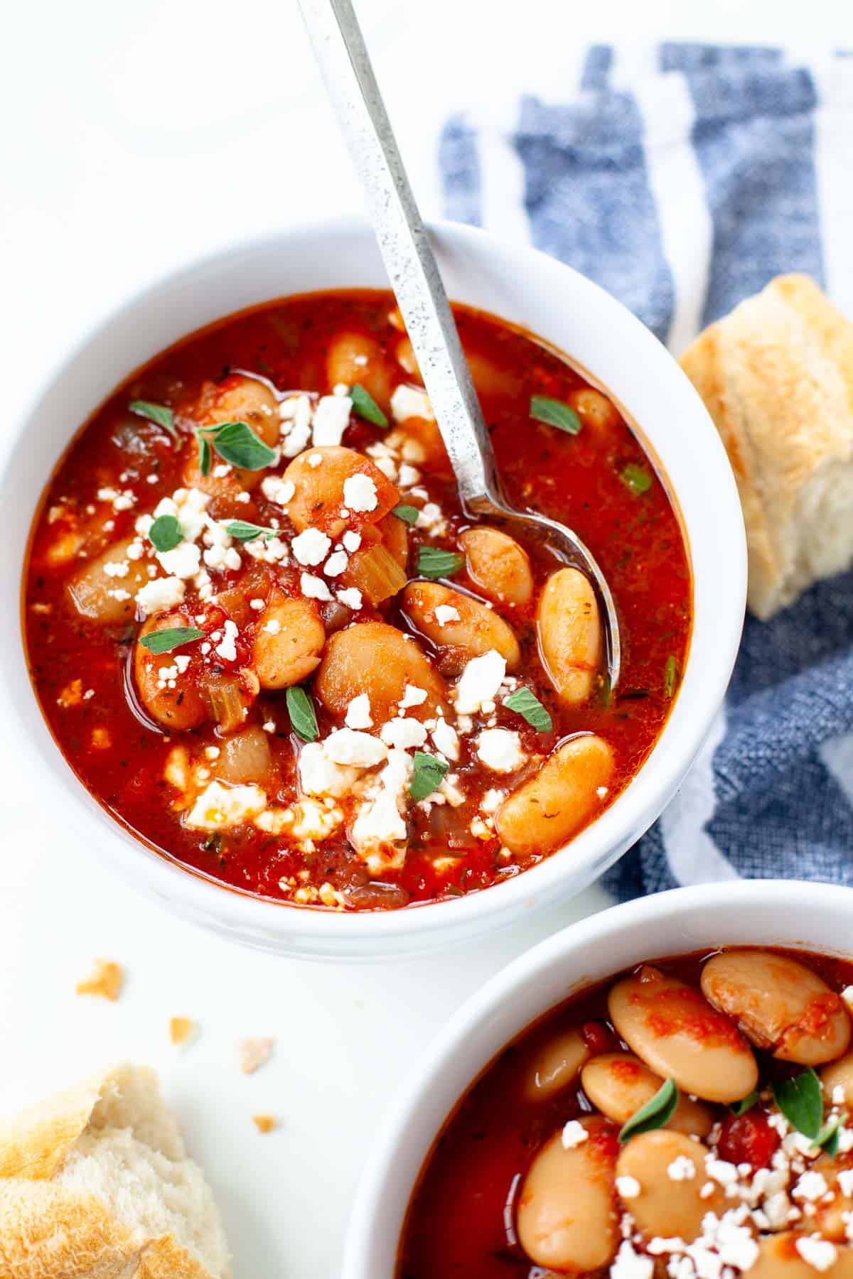 slow cooker greek baked beans in white bowl with spoon blue napkin bread feta cheese garnish