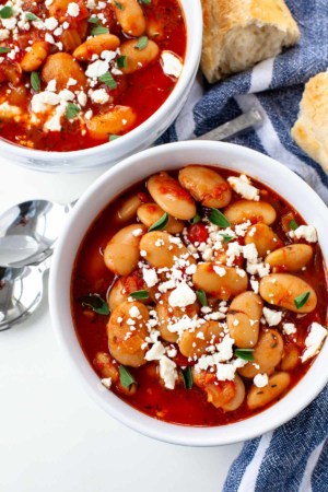 slow cooker greek baked beans in two white bowls feta cheese garnish blue napkin background