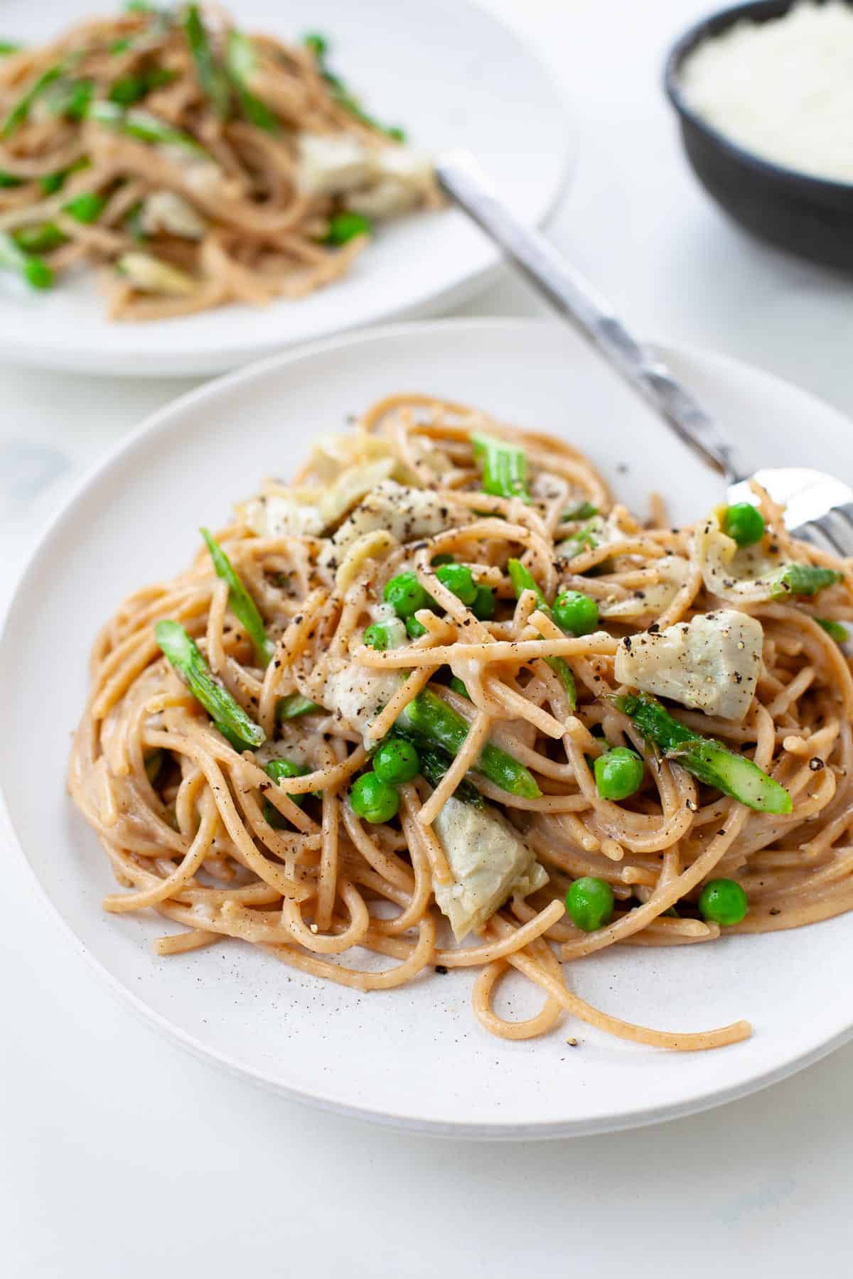spring vegetable pasta with asparagus, peas, artichokes on white plate with fork white background