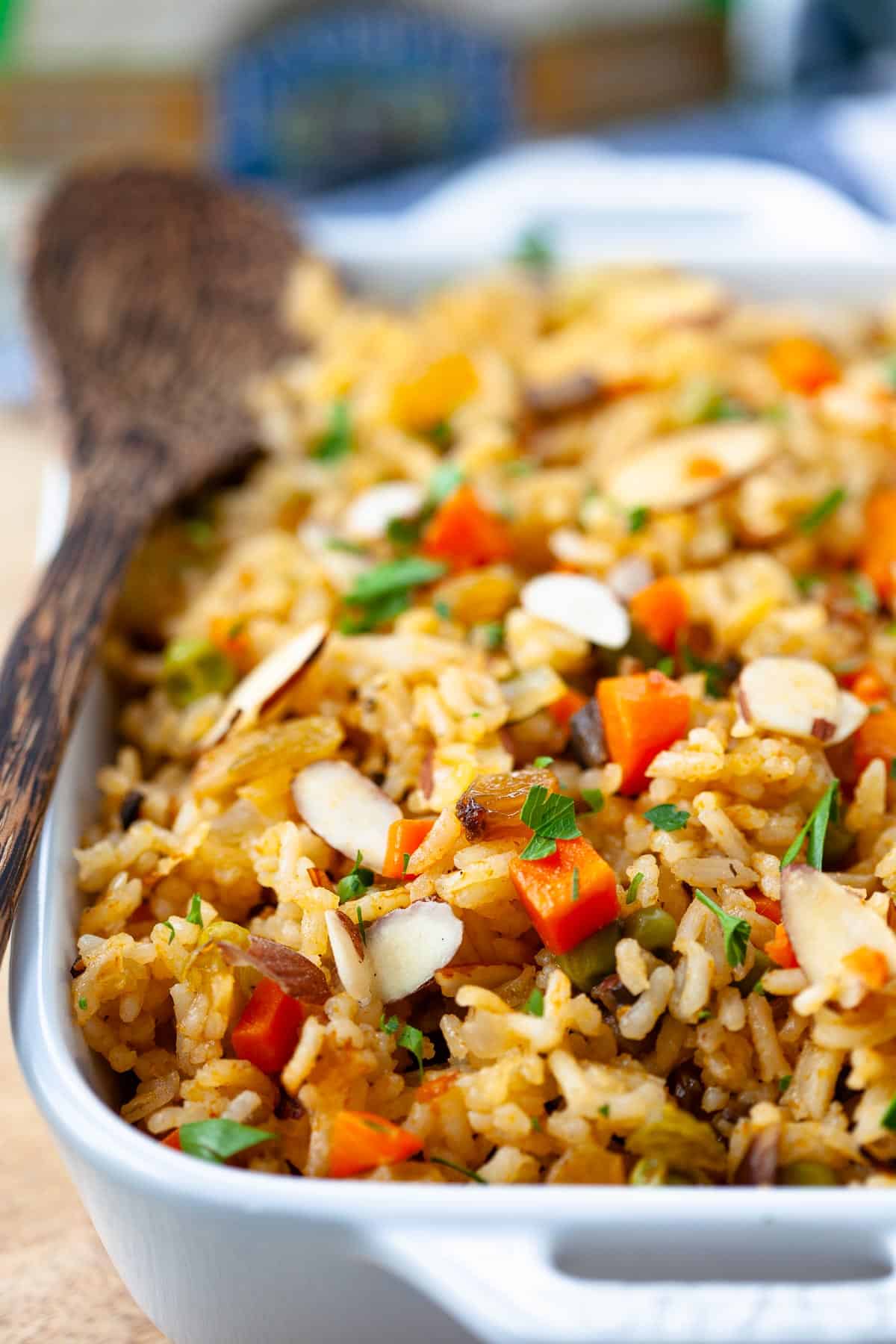 vegetarian rice pilaf casserole dish with wooden spoon long grain white rice, sliced almonds, golden raisins