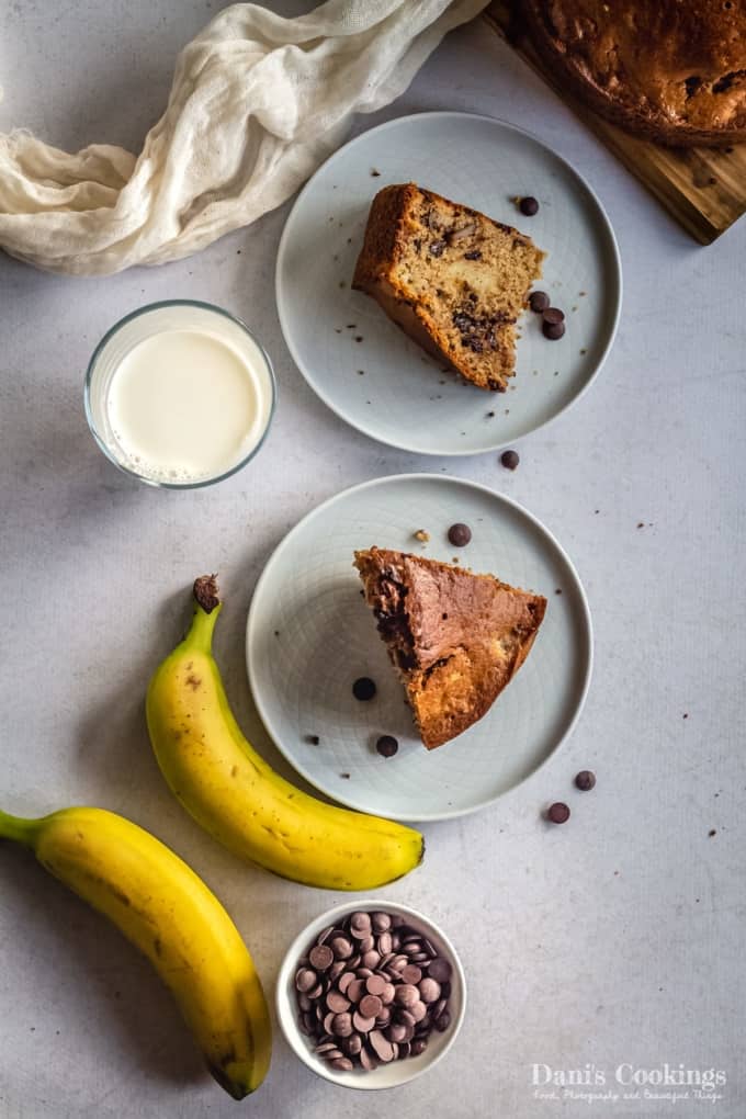 two slices of banana bread on plates, bananas and chocolate chips on the side