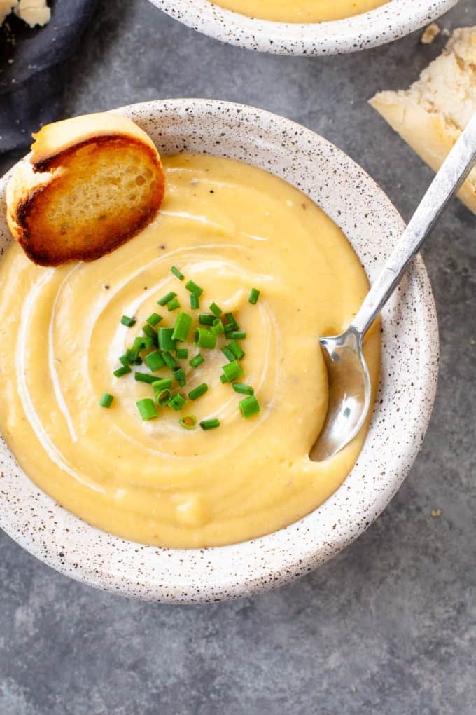 Bowl of creamy potato leek soup with a slice of toasted baguette, sprinkle of chives