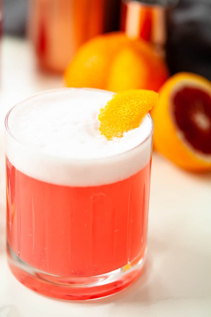 Close up of pink cocktail in rocks glass, white foam, orange rind garnish
