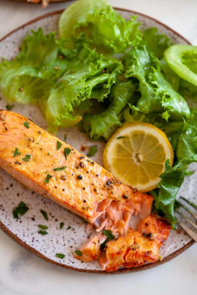 air fryer salmon on plate, small side salad, bite taken out of salmon