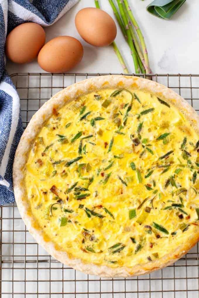 Baked whole quiche, white marble, whole eggs and asparagus in the background