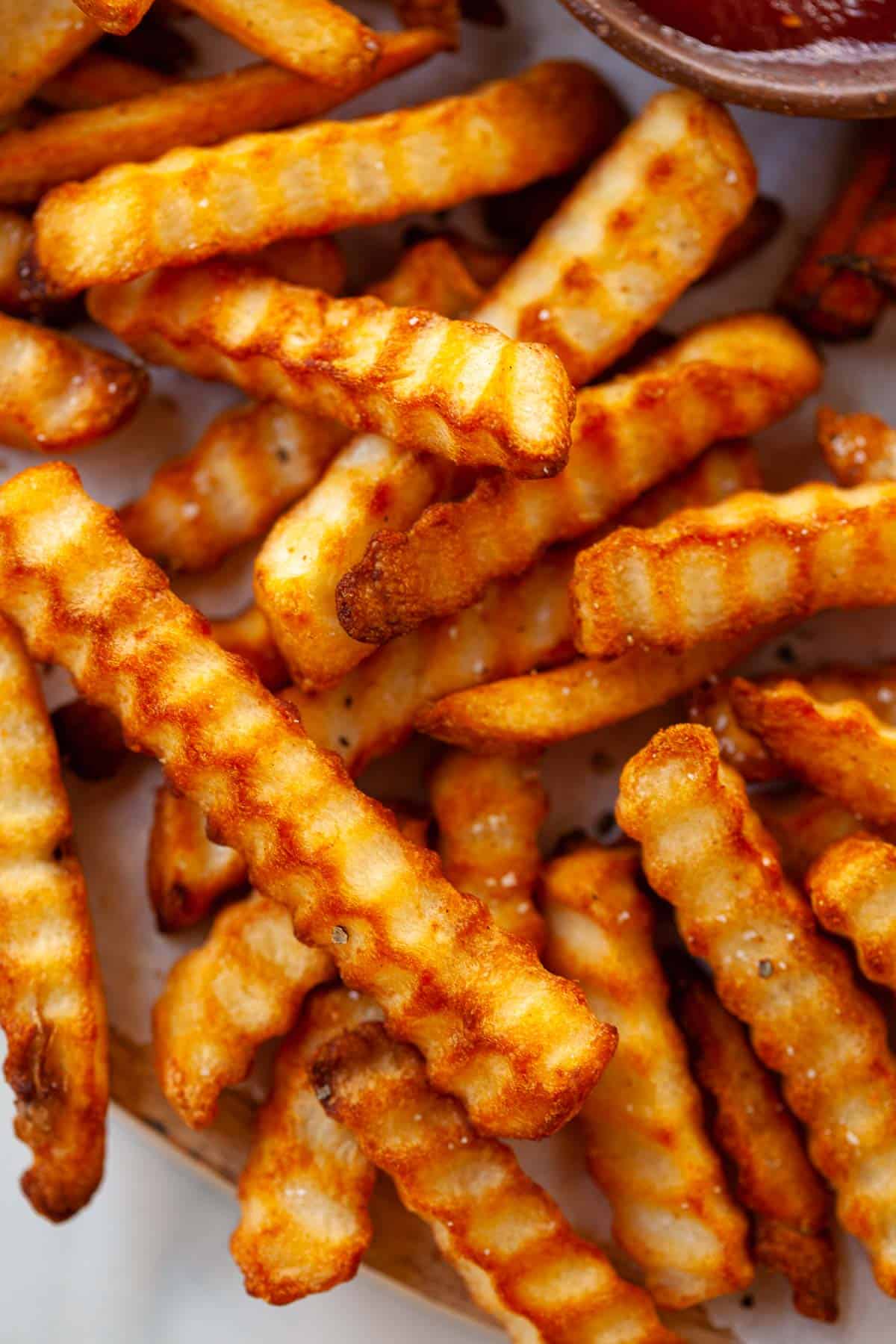 close up. crispy, golden crinkle fries. sprinkle of salt. on white napkin.