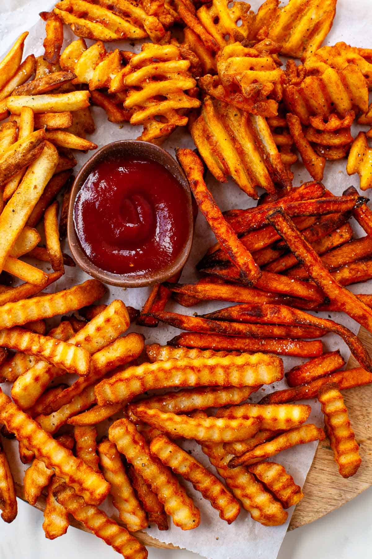ketchup in small wooden bowl. crispy crinkle, sweet potato, regular, and waffle fries. on a white napkin.