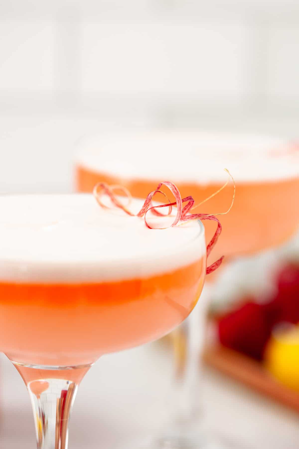 two strawberry rhubarb cocktails in coupe glasses with curly rhubarb peel garnish 