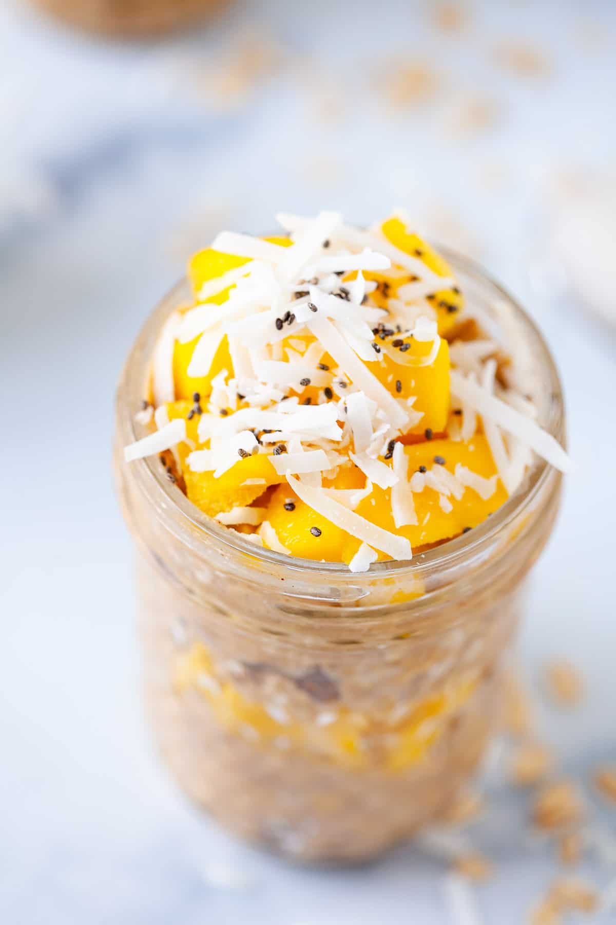 close up. overnight oats in mason jar. topped with. mango chunks. coconut shreds. chia seeds.