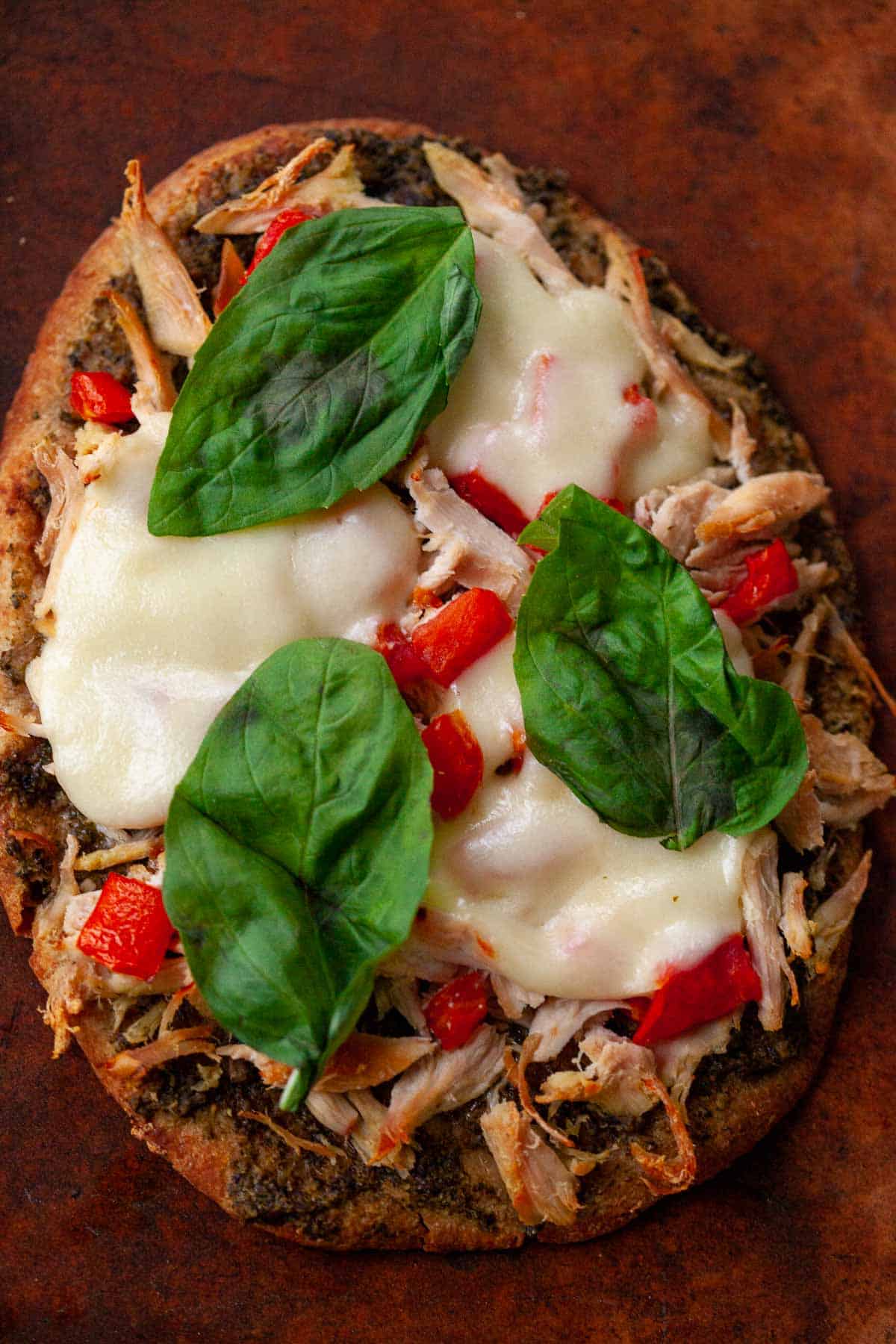 whole wheat naan flatbread with chicken, pesto, cheese, tomatoes, basil on brown pizza stone
