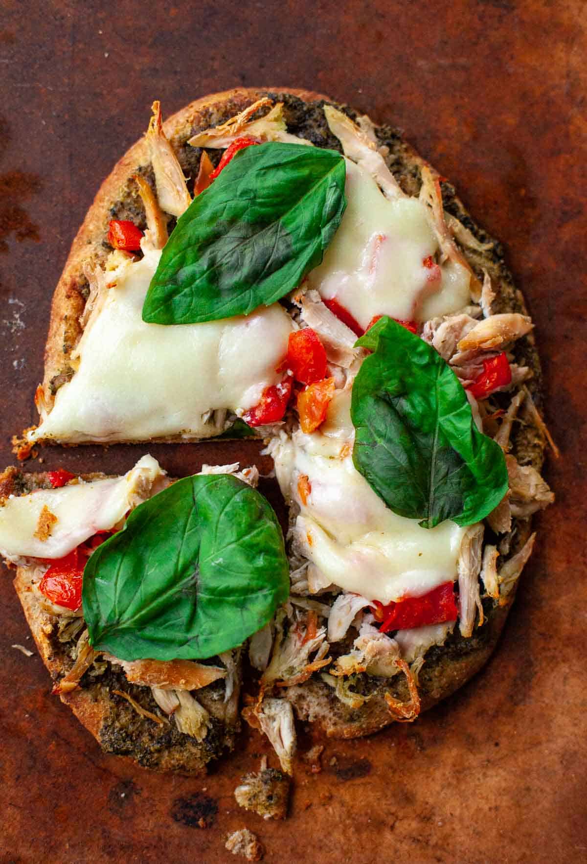 Hähnchen-Pesto-Fladenbrot mit Mozzarella-Tomaten-Basilikum auf Pizzastein mit einer Scheibe geschnitten 